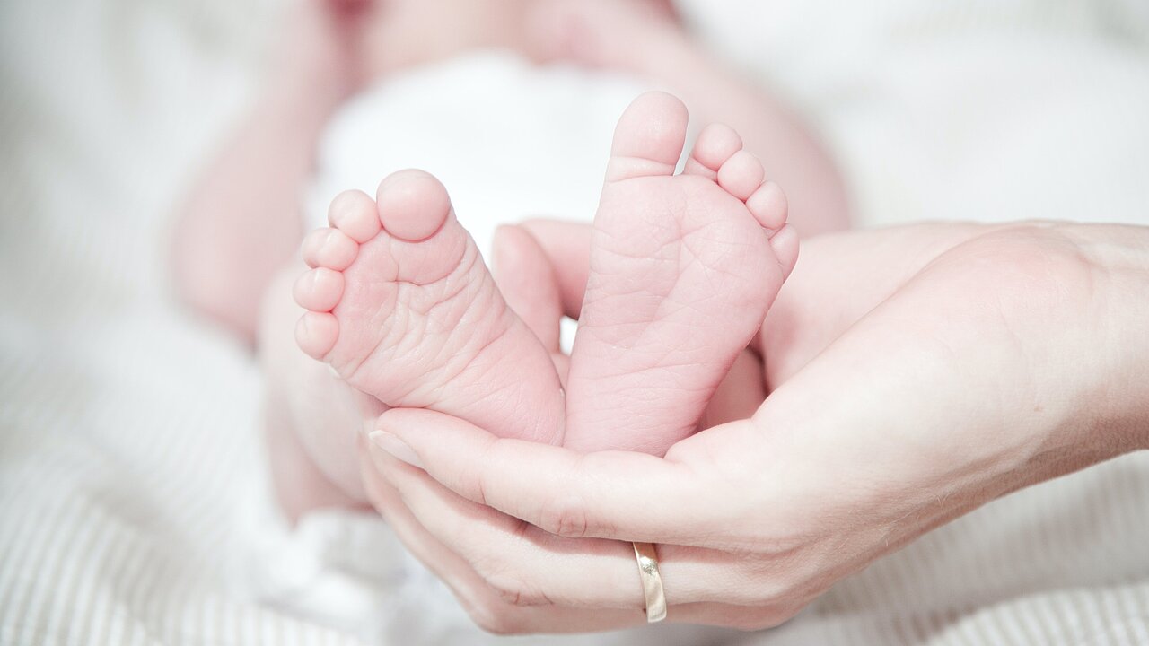 Die Hand einer Frau hält die Füße ihres Babys